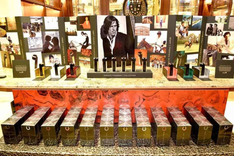 A display of luxury perfumes in elegant bottles, each set in front of a box, with a backdrop featuring a large black-and-white portrait and several smaller lifestyle photos.