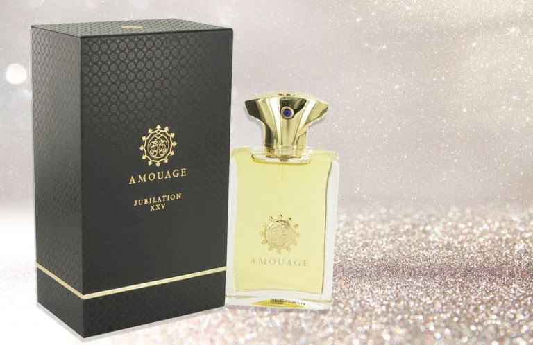 A bottle of Amouage Jubilation XXV perfume with a gold cap stands next to its elegant black and gold box against a sparkling, glittery background.