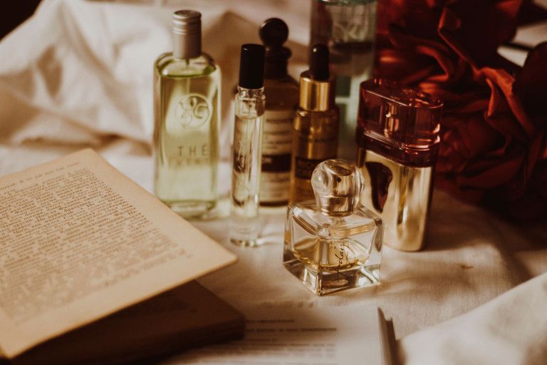 A collection of perfume bottles in different sizes and concentrations beside an open book, in warm light