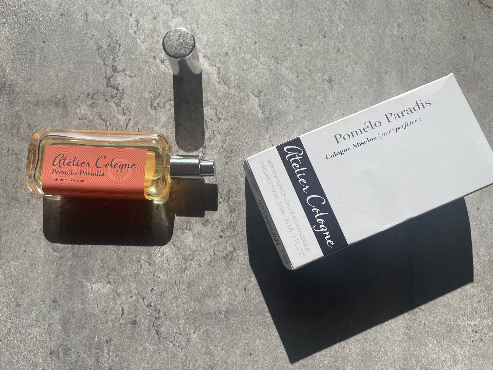 Atelier Cologne Pomelo Paradis Review: The Grapefruit That Stays Atelier Cologne Pomelo Paradis bottle and box on concrete with hard afternoon shadows