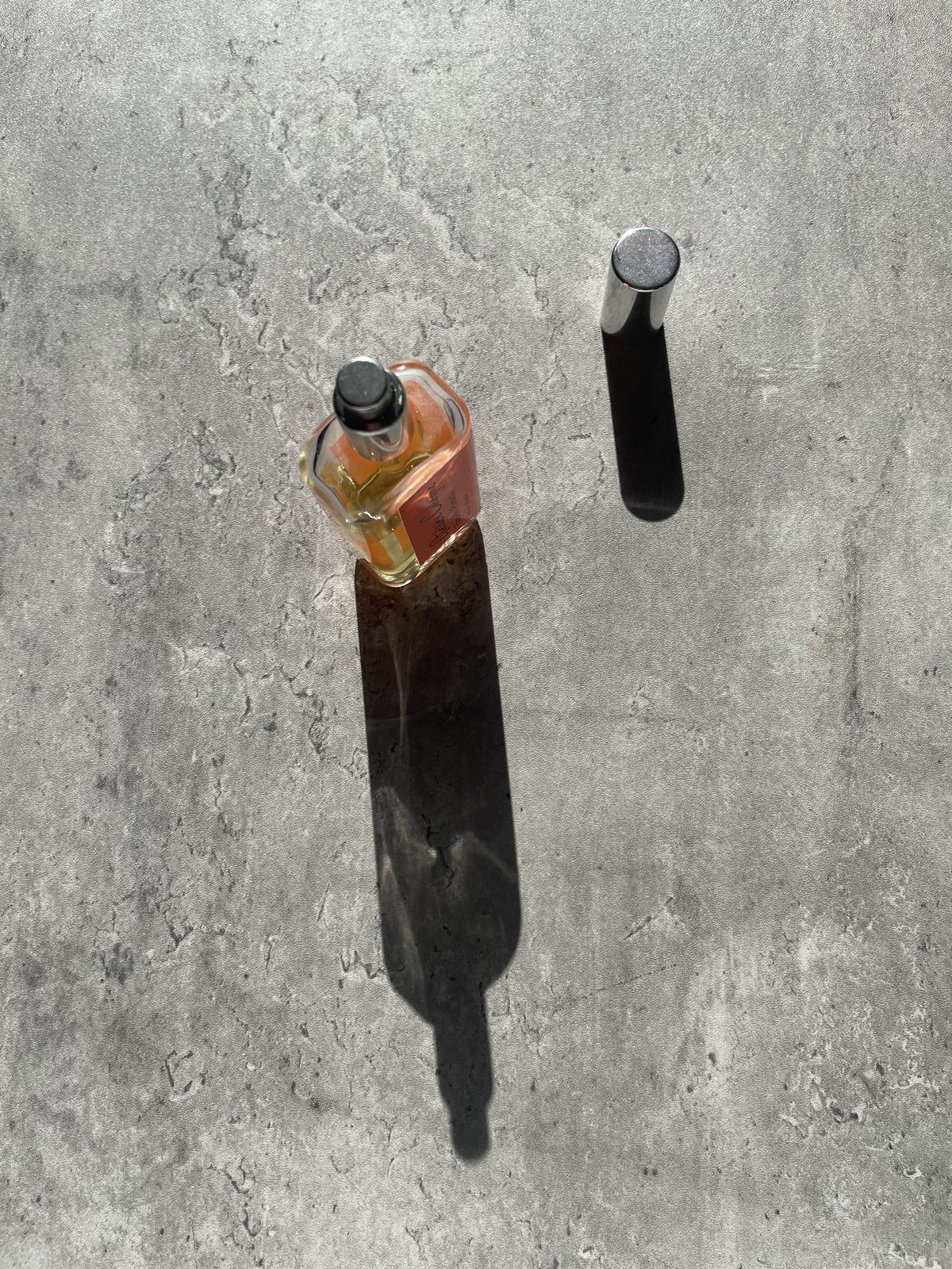 Atelier Cologne Pomelo Paradis Review: The Grapefruit That Stays Atelier Cologne Pomelo Paradis with the silver cap removed, both casting long shadows on concrete