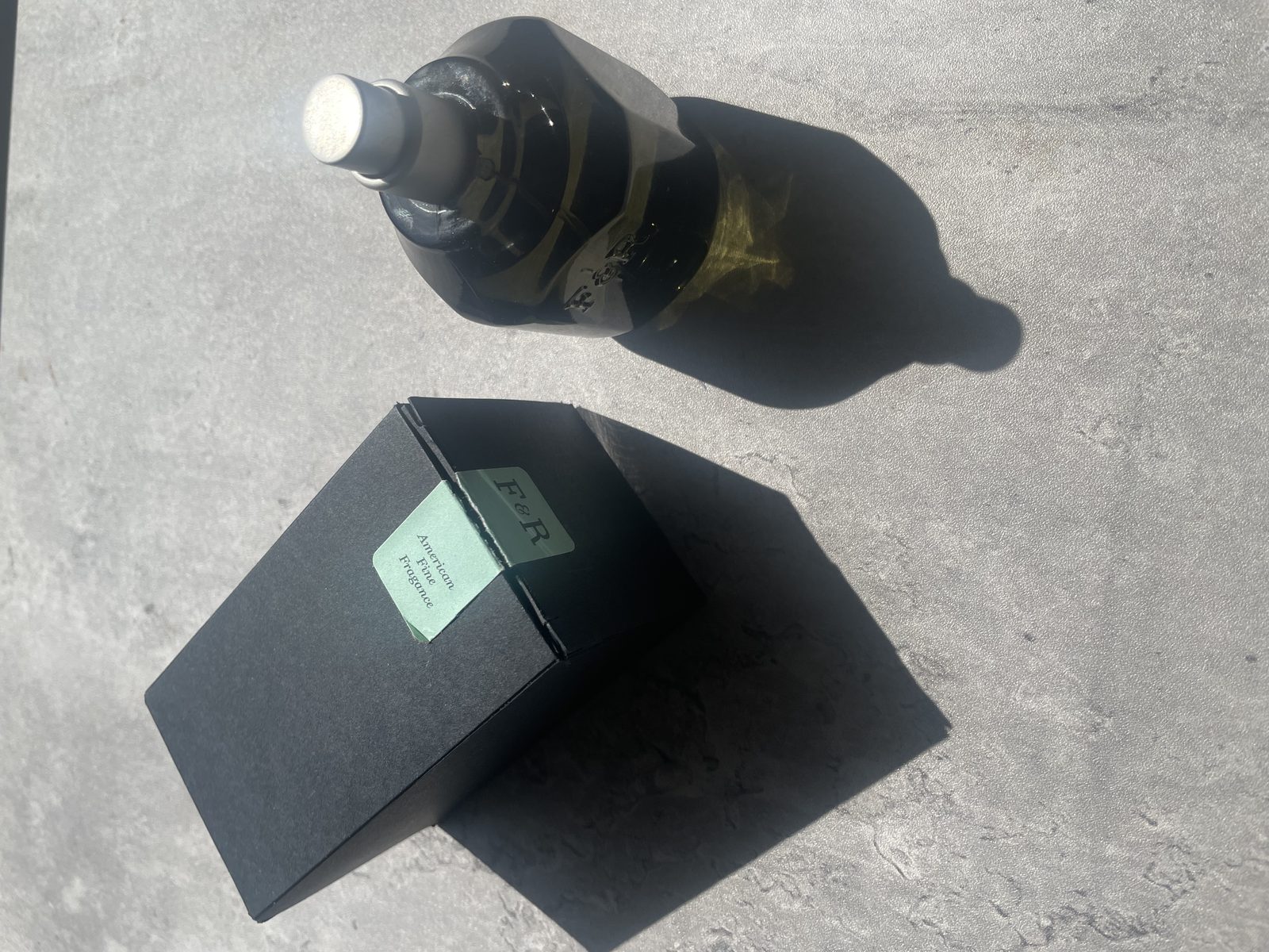 Fulton & Roark Mahana Review: The Same Missing Word as Cloudland Fulton & Roark Mahana bottle on concrete, the smoked olive glass reading almost black in hard sun