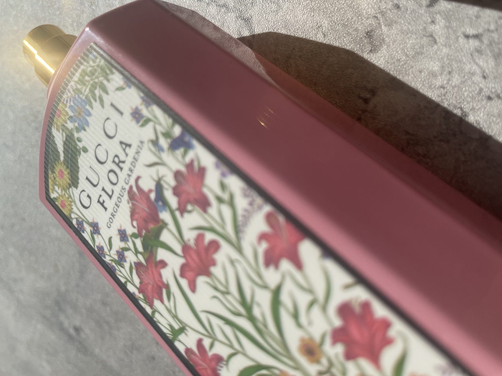 Gucci Flora Gorgeous Gardenia Review: The Flower That Isn't There Abstract close crop of the ribbed gold Gucci cap against the pink lacquered glass
