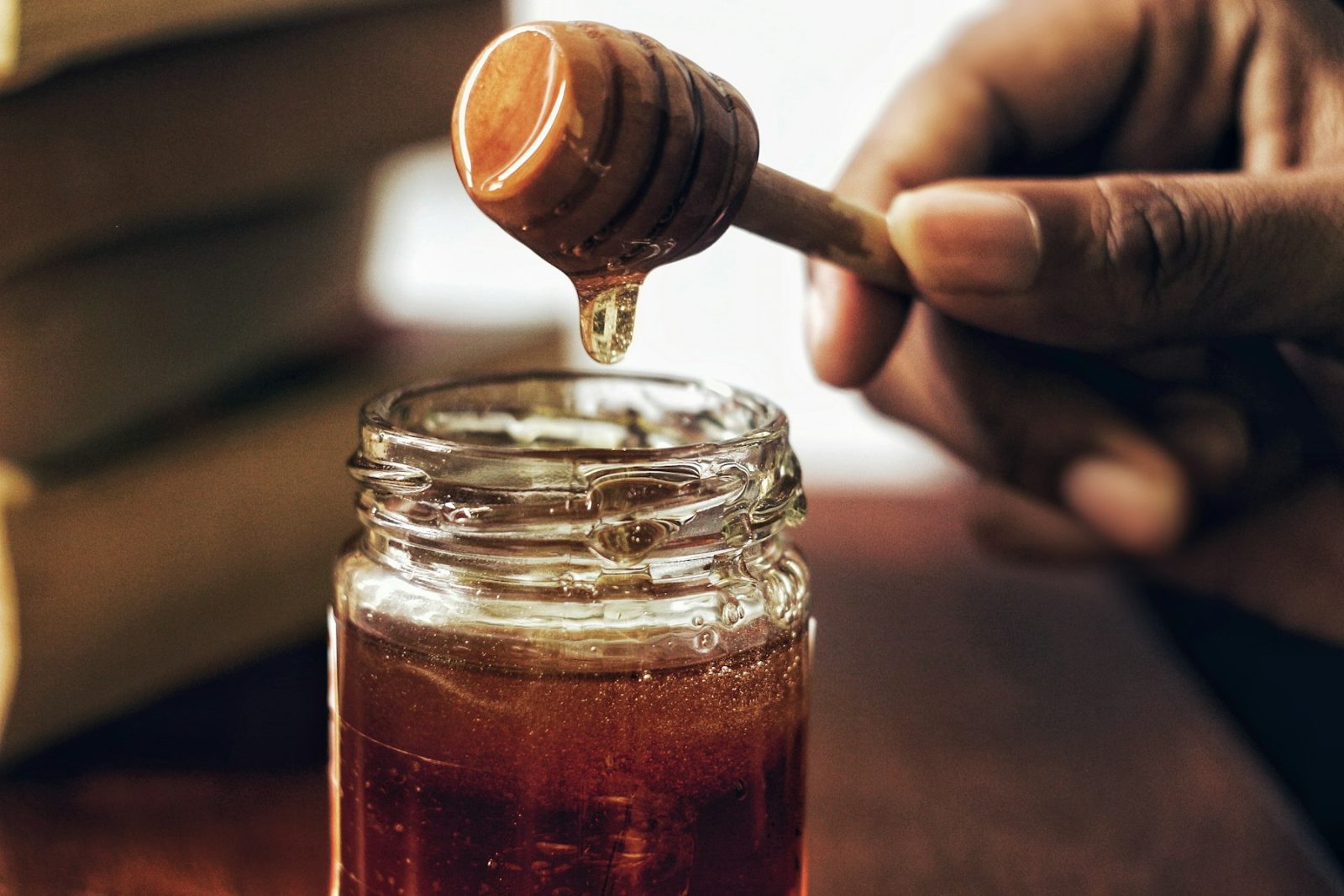 What Does Honey Smell Like? A wooden dipper lifting golden honey above an open glass jar