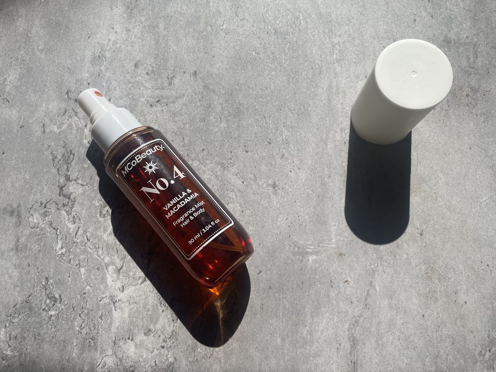 MCoBeauty No.4 Vanilla & Macadamia Review: What the Back Panel Says MCoBeauty No.4 lying on concrete with the amber juice throwing a warm shadow