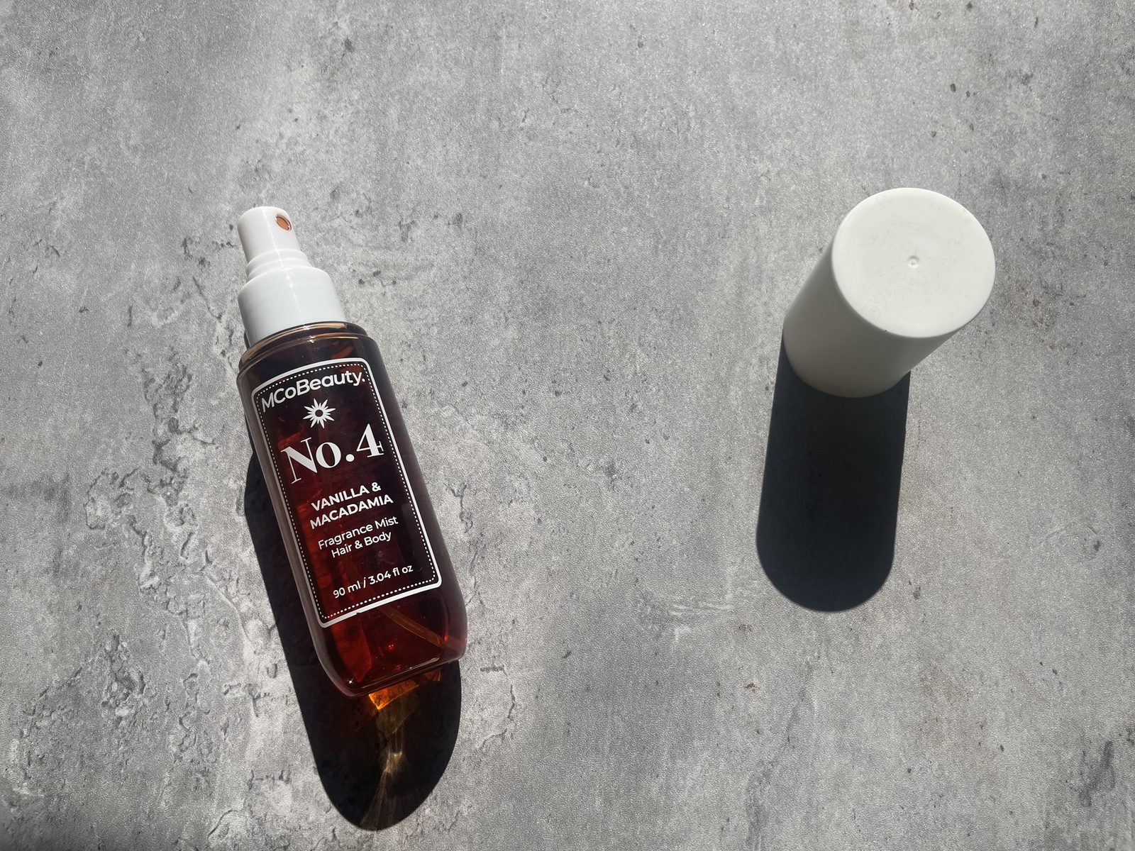 MCoBeauty No.4 Vanilla & Macadamia Review: What the Back Panel Says MCoBeauty No.4 Vanilla & Macadamia fragrance mist on sunlit concrete beside its white cap