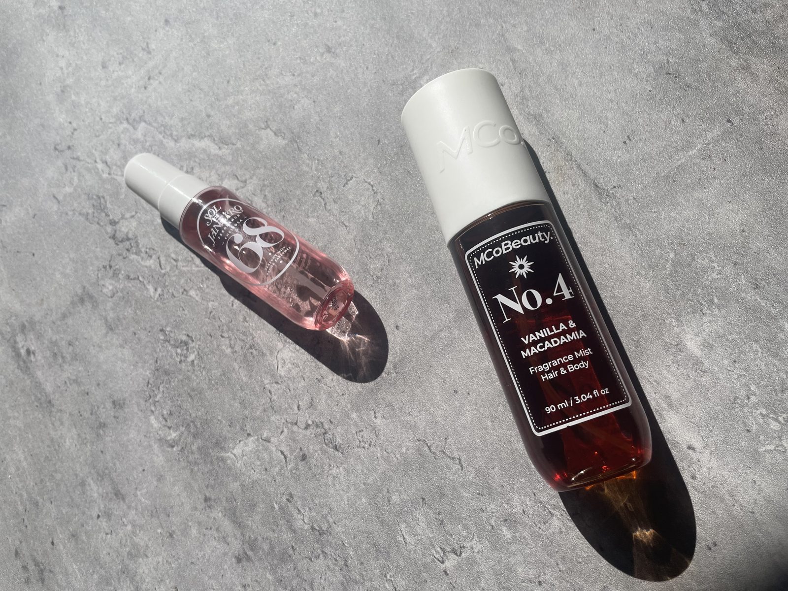 MCoBeauty vs Sol de Janeiro: I Own Both, and They Don't Smell Alike MCoBeauty No.4 and Sol de Janeiro Cheirosa 68 laid diagonally on concrete with their shadows