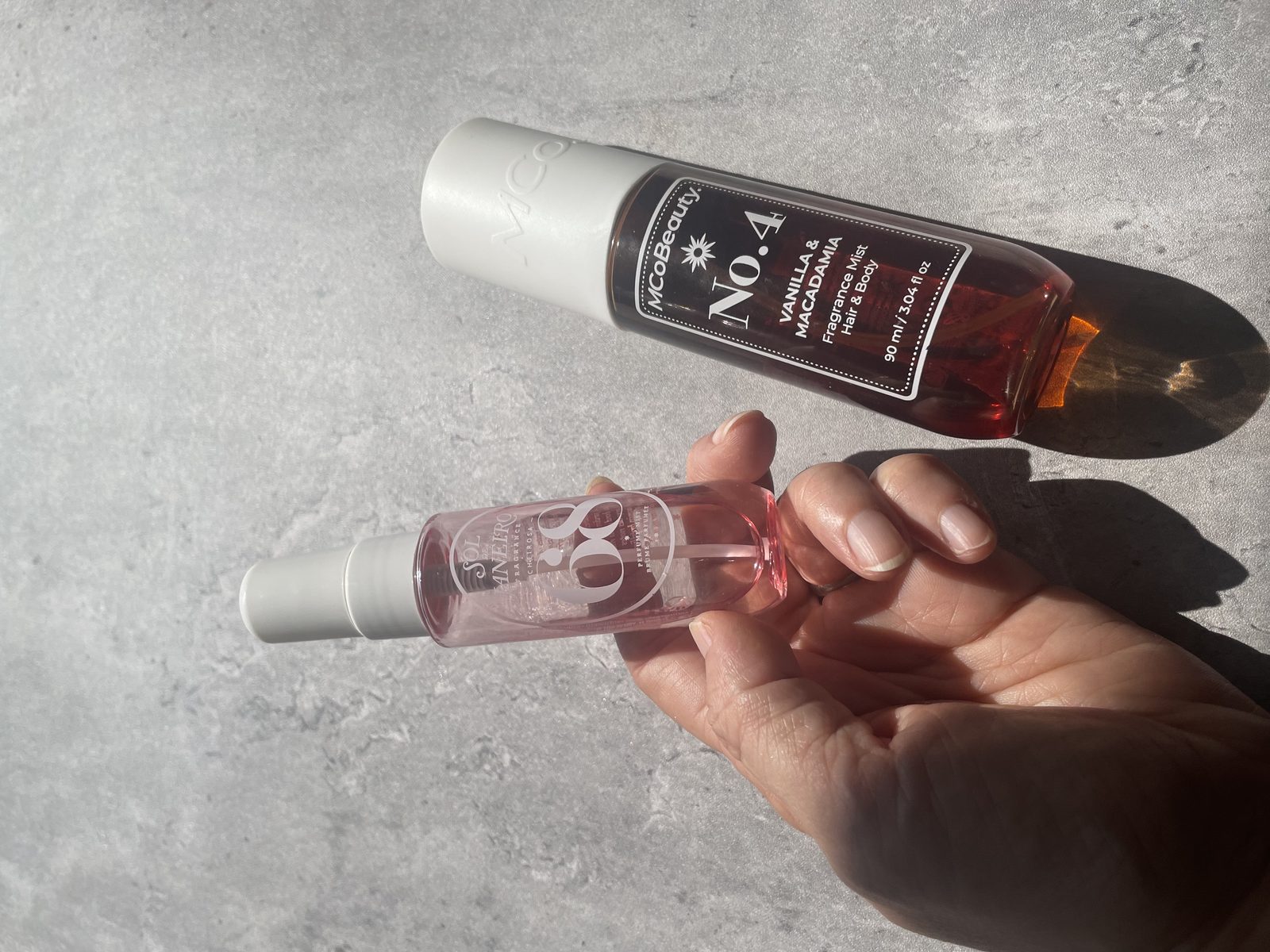 MCoBeauty vs Sol de Janeiro: I Own Both, and They Don't Smell Alike MCoBeauty No.4 Vanilla & Macadamia and Sol de Janeiro Cheirosa 68 on sunlit concrete, both labels readable