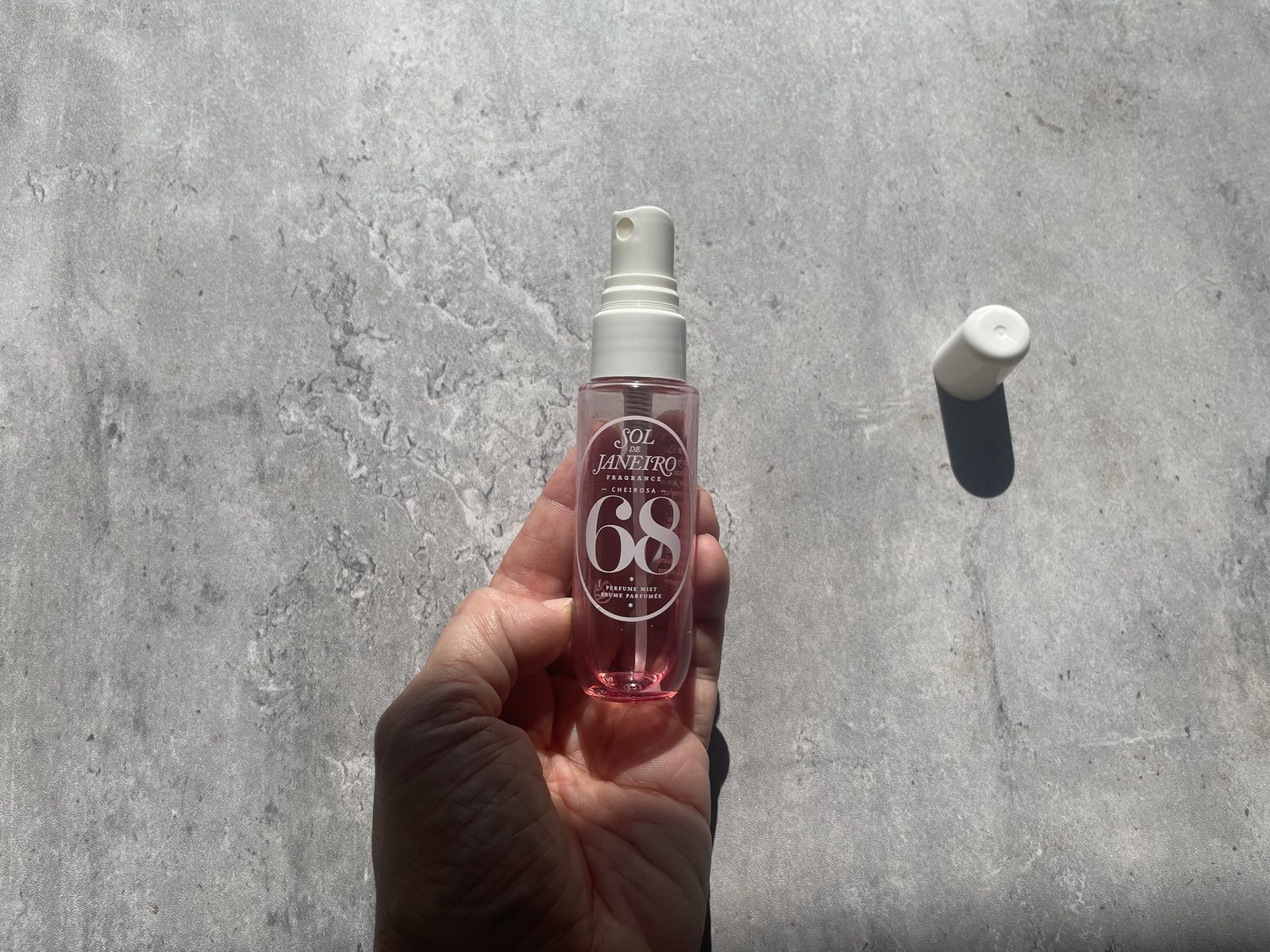 Sol de Janeiro Cheirosa 68 Review: The One That Isn't Pistachio Sol de Janeiro Cheirosa 68 perfume mist held in hand on sunlit concrete, cap off beside it