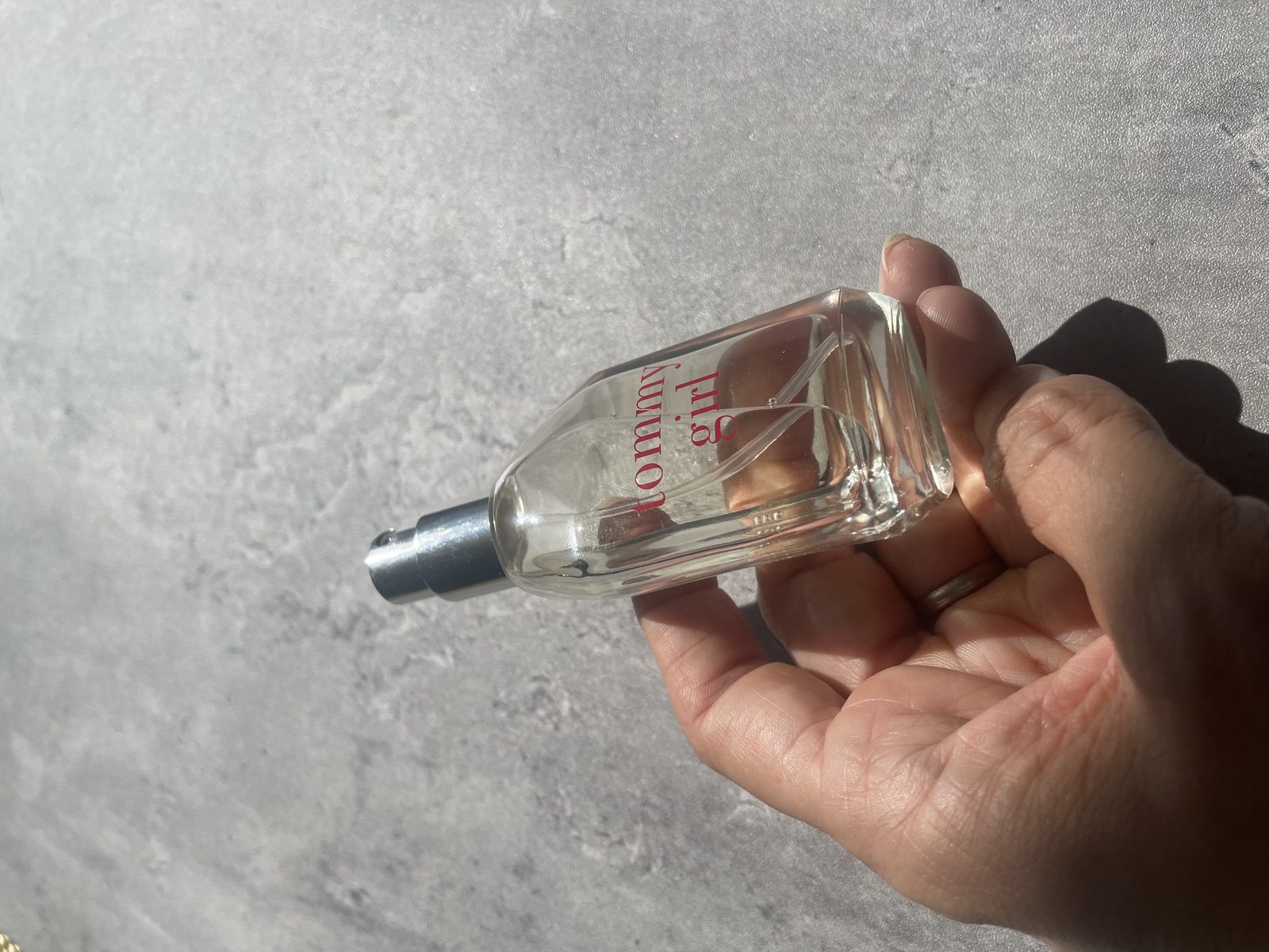 Is The Evocative Fragrance Of Tommy Girl Perfume For You? Holding the Tommy Girl Eau de Toilette bottle in sunlight, showing the red logo and silver sprayer