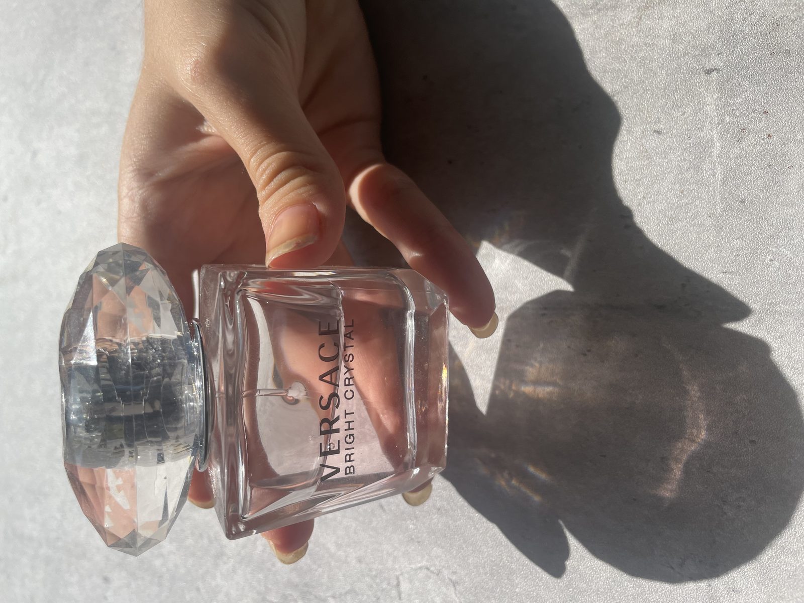 What Does Versace Bright Crystal Smell Like? Holding the Versace Bright Crystal bottle with the faceted crystal cap removed