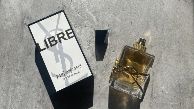 YSL Libre Eau de Parfum bottle and box on sunlit concrete, gold YSL logo facing camera