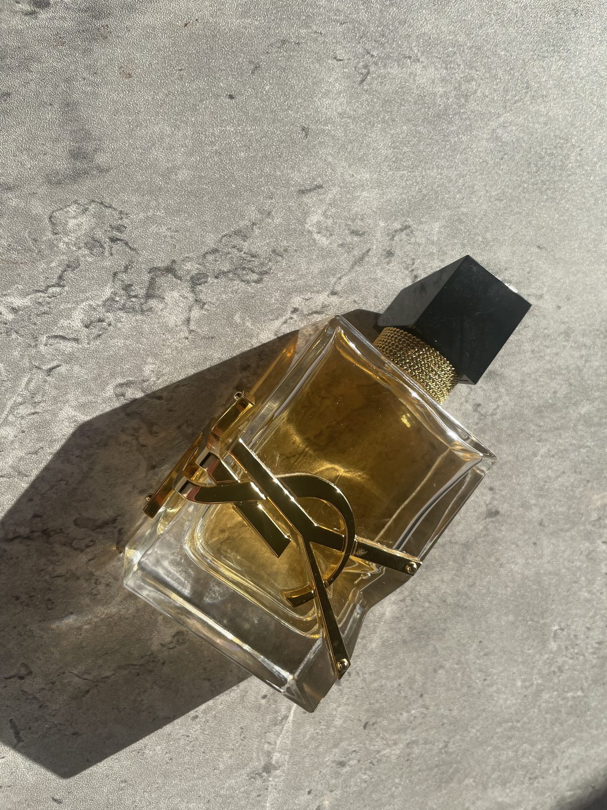 Bring On The Florals of Spring: YSL Libre Perfume Reviewed YSL Libre Eau de Parfum bottle with the black cap on, on a sunlit concrete surface